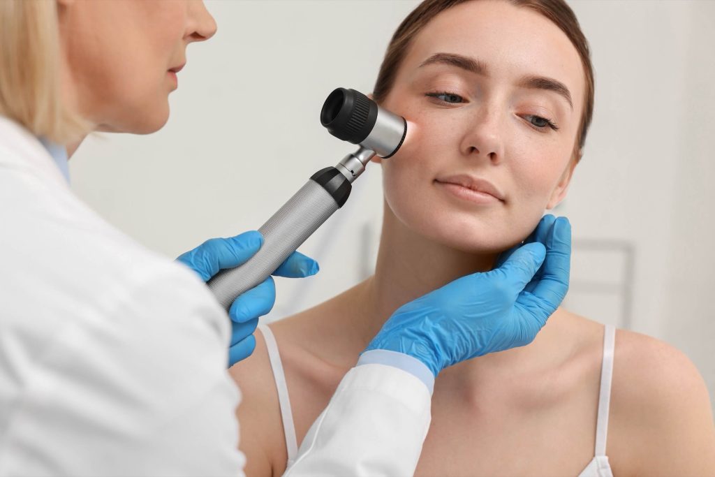 Dermatologist using a dermatoscope to examine a spot on a patient's face in a clinic.